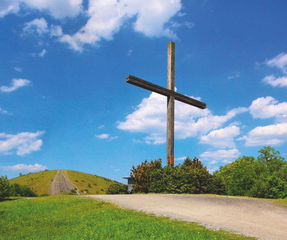 großes Holzkreuz am Weg mit blauem Himmel und Wolken.
